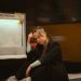 A young woman in casual attire seated at a Berlin subway station with trains in motion.