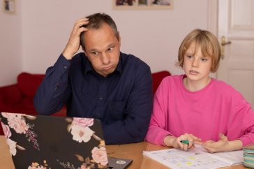 A father and daughter working on a laptop, focusing on home education activities.