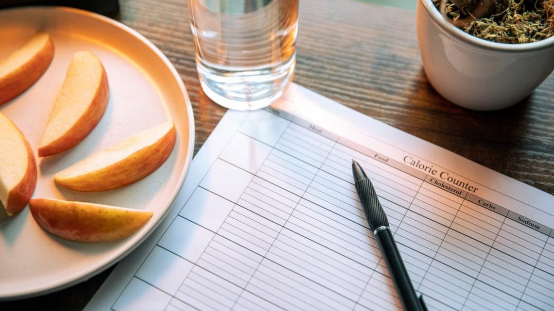 Flat lay featuring apple slices, a calorie counter chart, pen, and a glass of water for a healthy lifestyle.