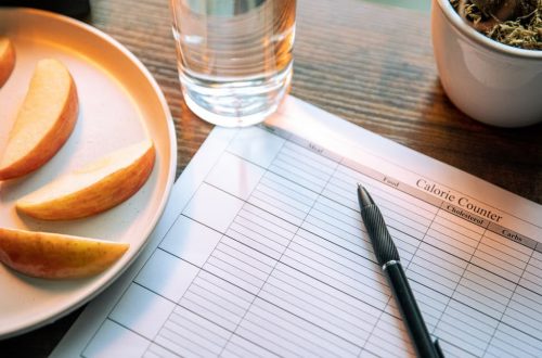 Flat lay featuring apple slices, a calorie counter chart, pen, and a glass of water for a healthy lifestyle.