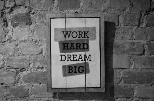Black and white frame with inspirational Work Hard Dream Big inscription hanging on brick wall