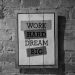 Black and white frame with inspirational Work Hard Dream Big inscription hanging on brick wall